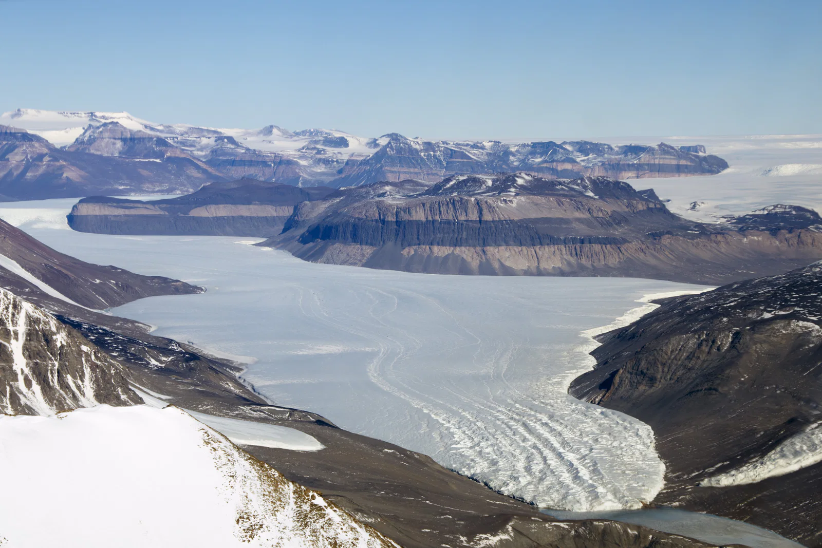 Aerial view of Taylor Glacier between bare Antarctic mountains, with a small dark Blood Falls stain near the lower-right.